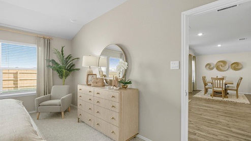Mesa Ridge model home primary bedroom with carpeted flooring and view of open concept living room.