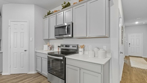 Mesa Ridge model home kitchen with light grey cabinets and granite countertops and view of entry way.