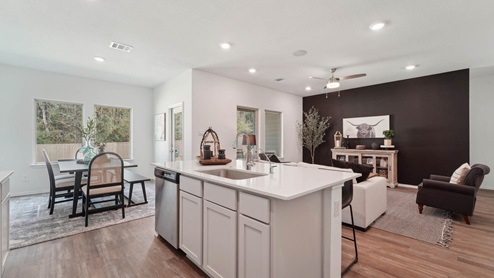 Open kitchen with an island, stainless steel appliances, white cabinets, white walls, and vinyl wood flooring.