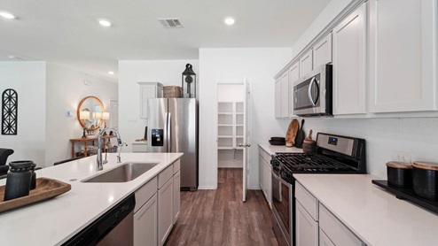 Open kitchen with an island, stainless steel appliances, white cabinets, white walls, and vinyl wood flooring.