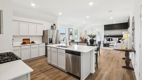 Open kitchen with an island, stainless steel appliances, white cabinets, white walls, and vinyl wood flooring.