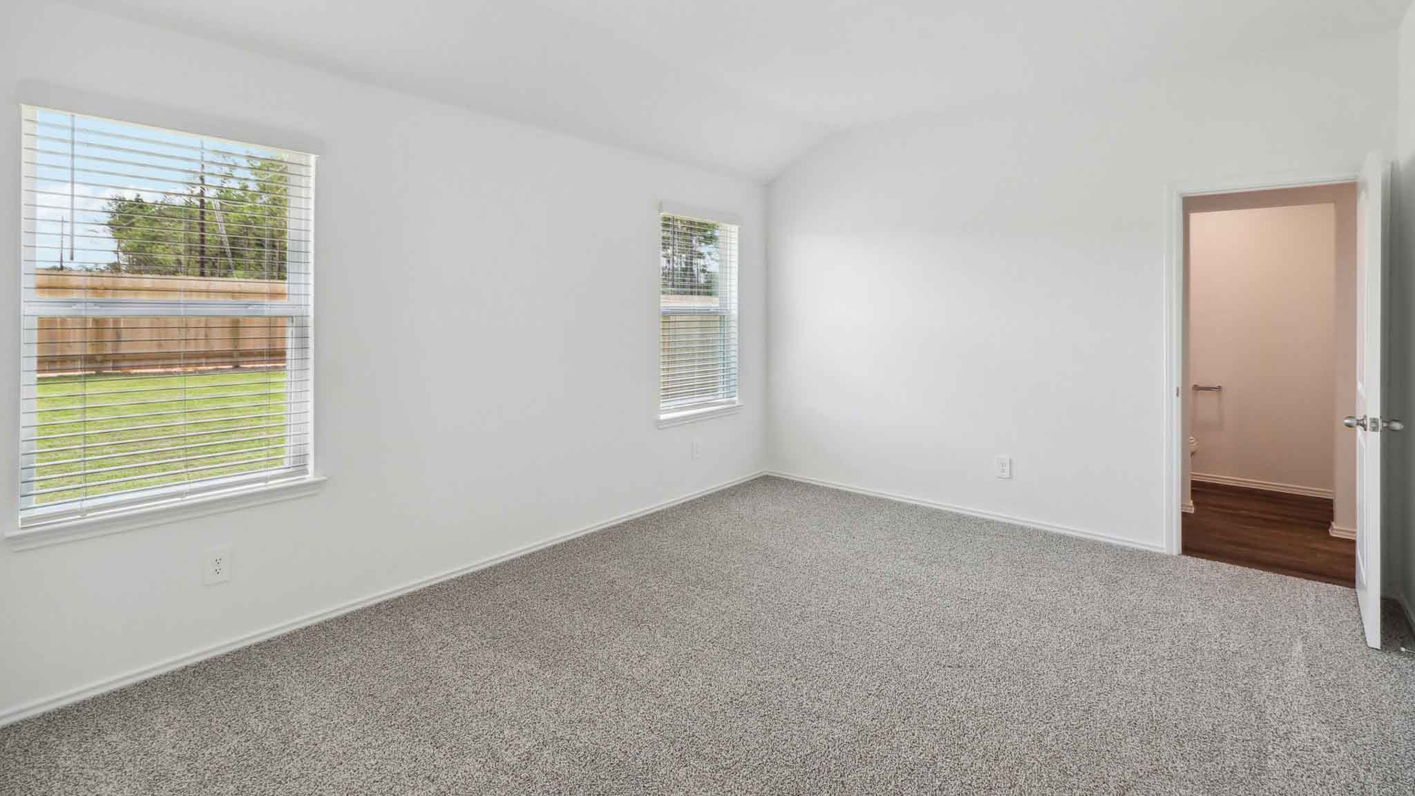 Primary bedroom with carpet flooring and two bright windows.