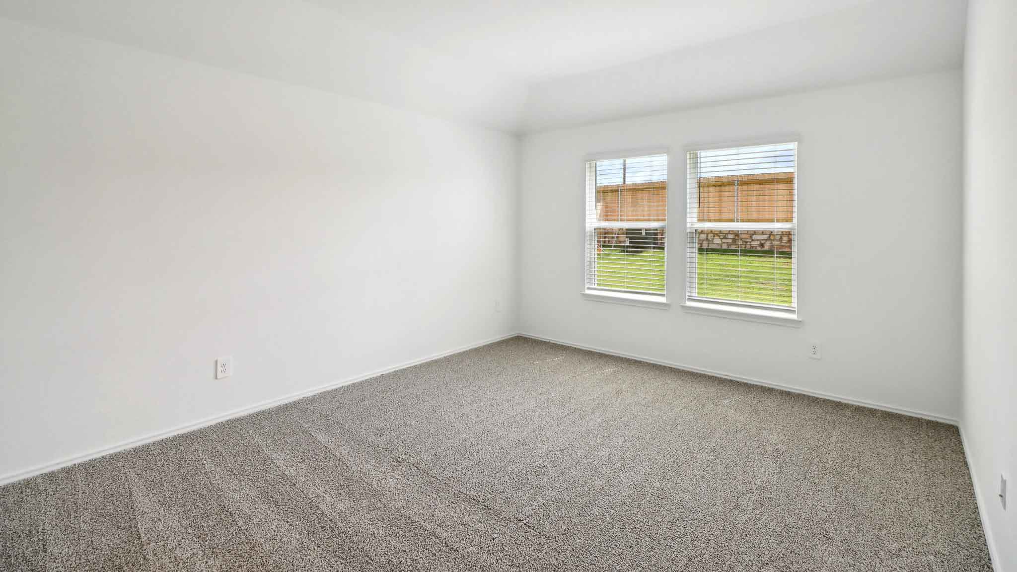 Primary bedroom with carpet flooring and two bright windows.