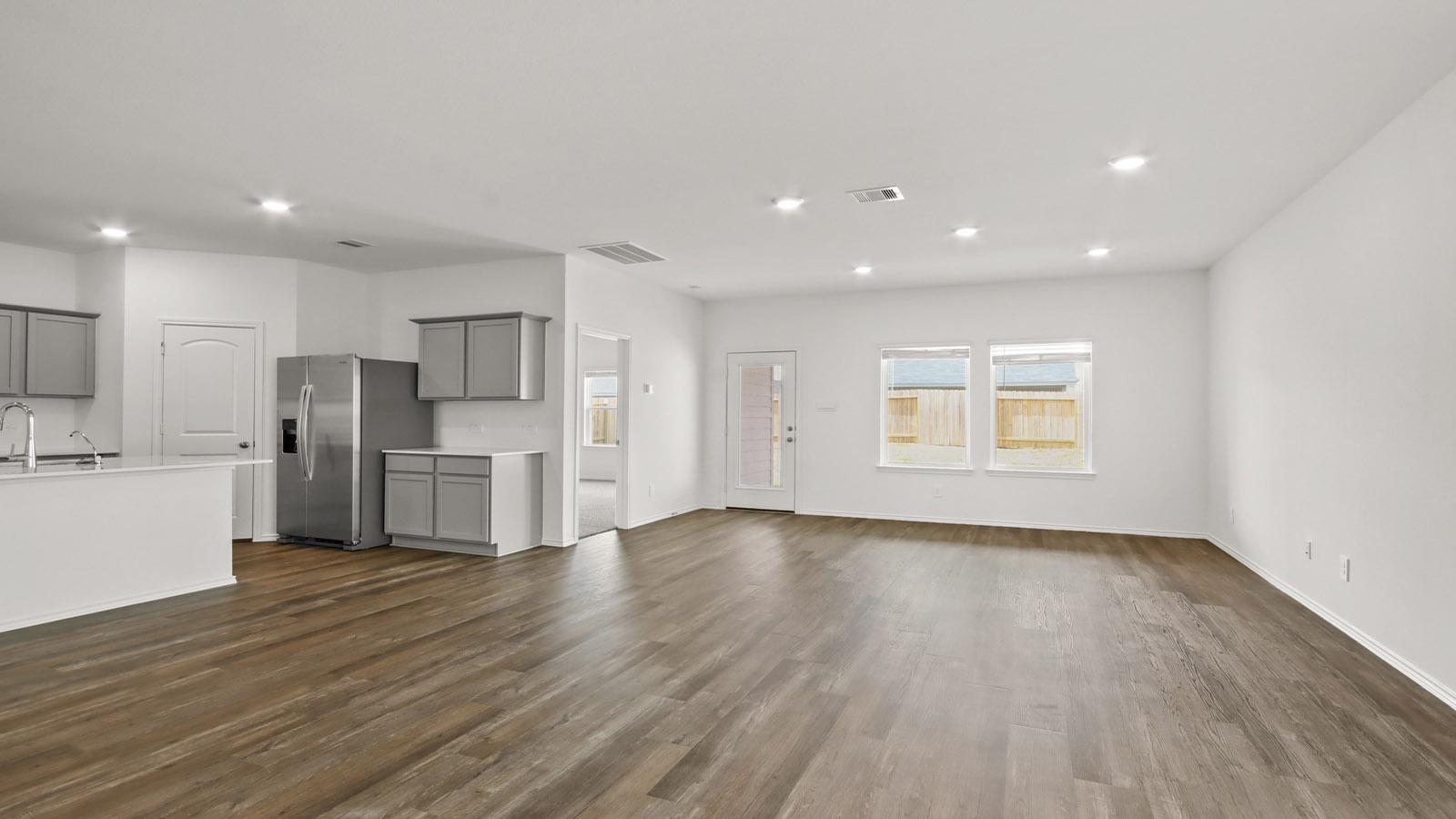 Open concept living, dining, and kitchen area with vinyl flooring and bright windows