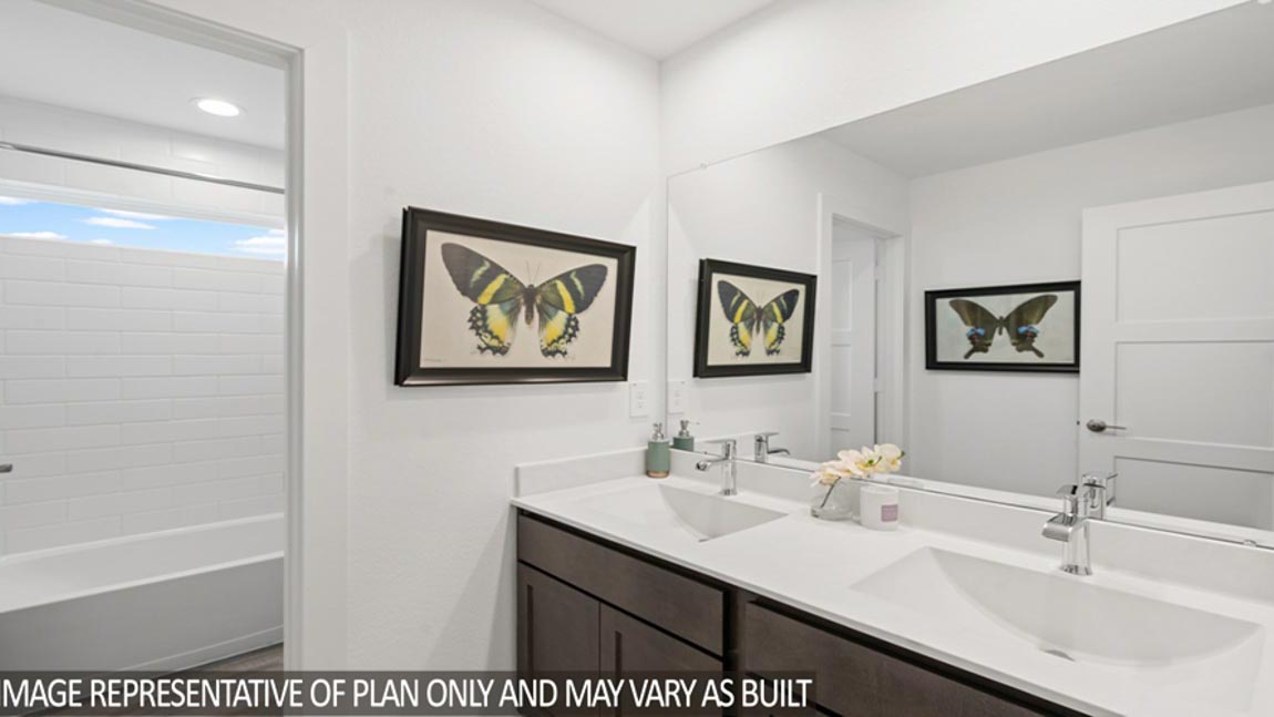 Secondary bathroom with dual sinks, shower and tub combo, white walls, and vinyl wood flooring.