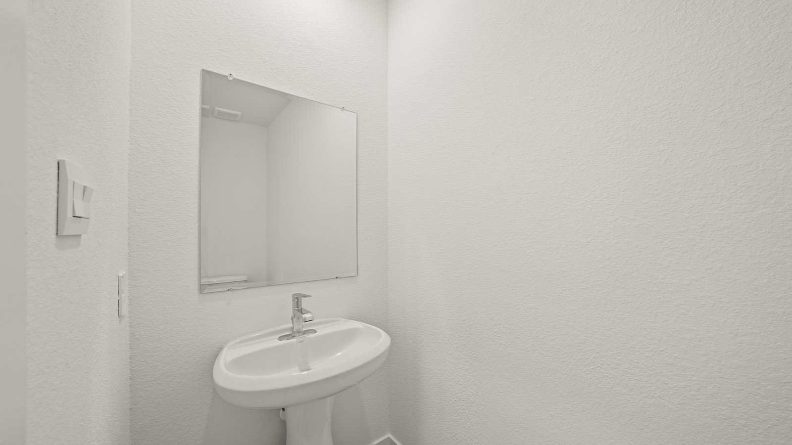 Half bath with door opening to hallway, pedestal sink, mirror visible with shiny faucet in The Arbor