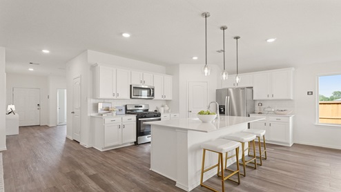 Open kitchen with an island, pendant lighting, back splash, white cabinets, white walls, and vinyl wood flooring.