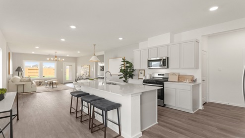 Open kitchen with an island, stainless steel appliances, white cabinets, white walls, and vinyl wood flooring.
