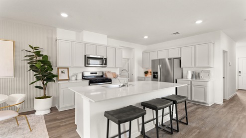 Open kitchen with an island, stainless steel appliances, white cabinets, white walls, and vinyl wood flooring.