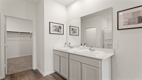 Secondary bathroom with dual sinks, shower and tub combo, white walls, and vinyl wood flooring.