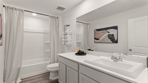 Secondary bathroom with dual sinks, shower and tub combo, white walls, and vinyl wood flooring.