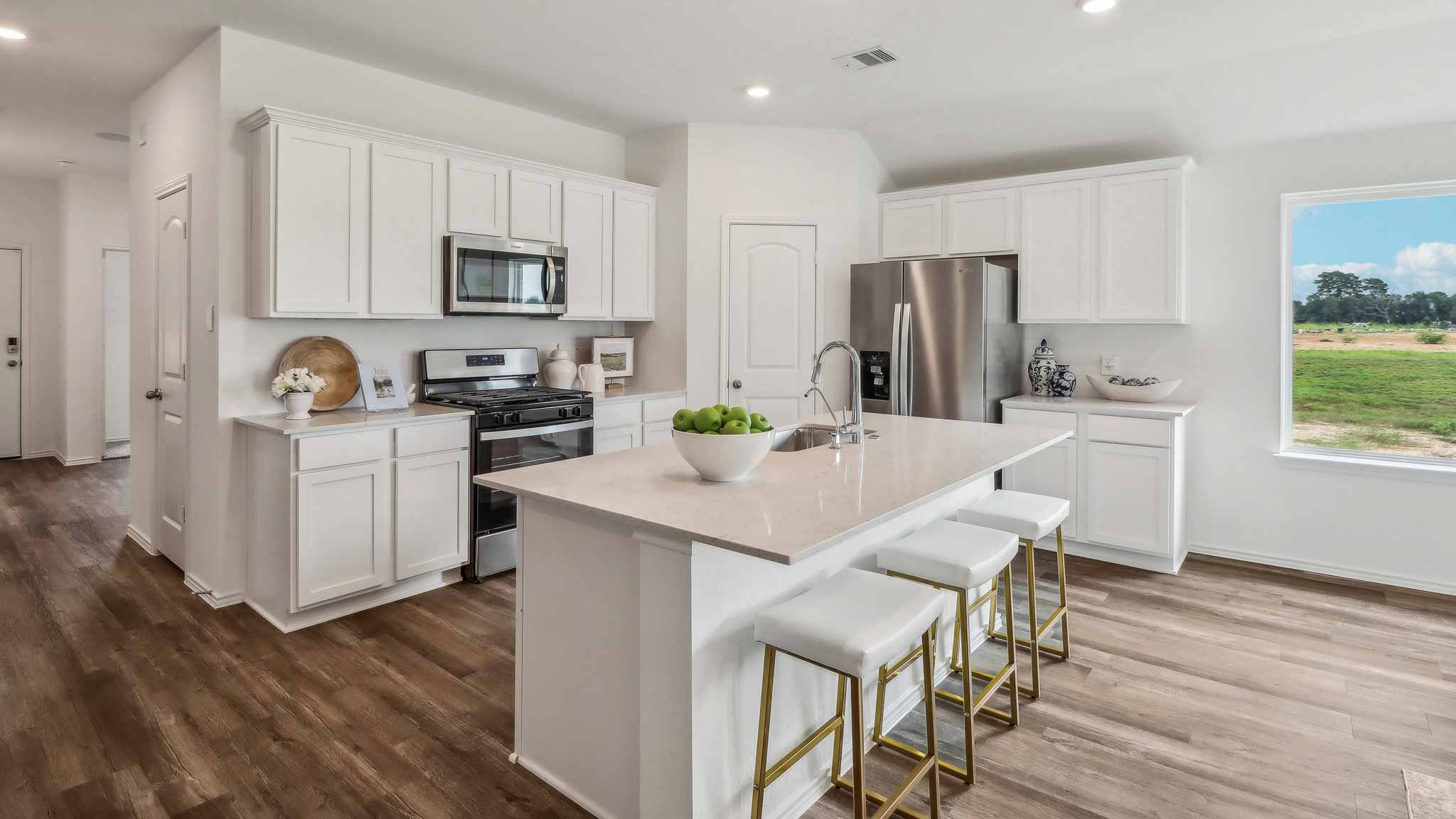 Open kitchen with an island, stainless steel appliances, white cabinets, white walls, and vinyl wood flooring.