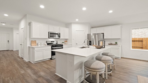 Open kitchen with an island, stainless steel appliances, white cabinets, white walls, and vinyl wood flooring.
