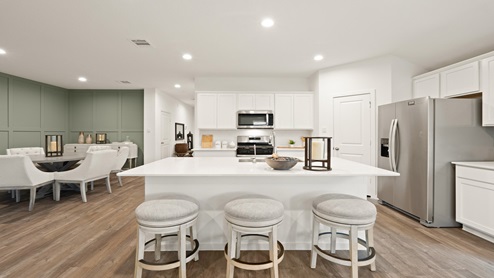 Open kitchen with an island, stainless steel appliances, white cabinets, white walls, and vinyl wood flooring.