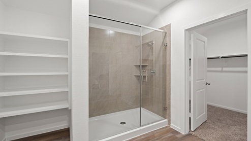 Primary bathroom with dual sinks, walk-in shower, storage shelves, white walls, and vinyl wood flooring.