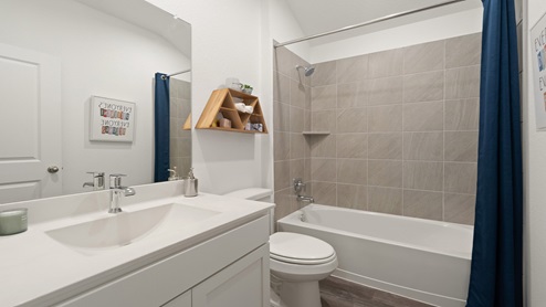 Secondary bathroom with a shower and tub combo, white walls, and vinyl wood flooring.