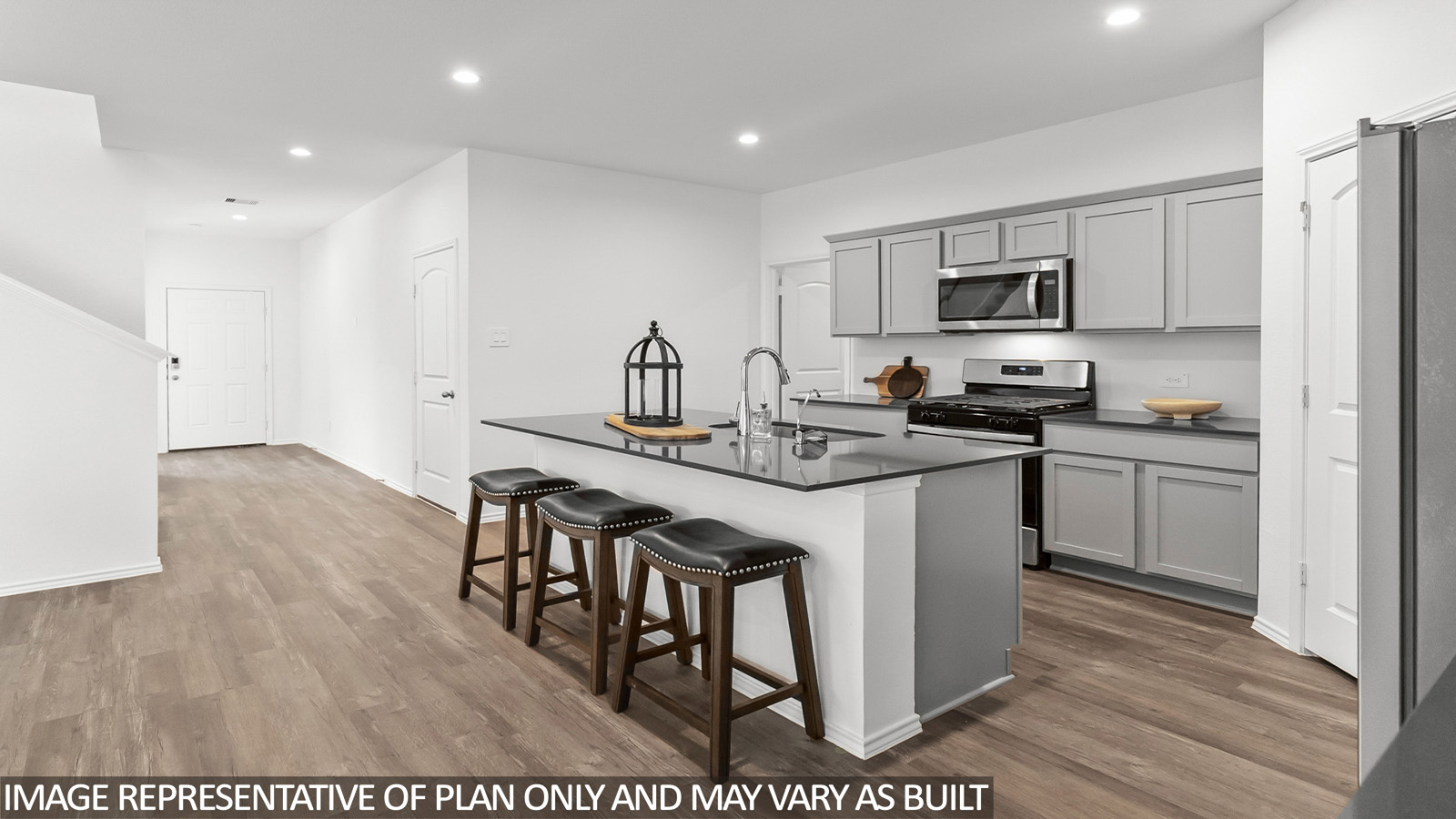 Open kitchen with an island, stainless steel appliances, light gray cabinets, white countertops, white walls, and vinyl wood flooring.