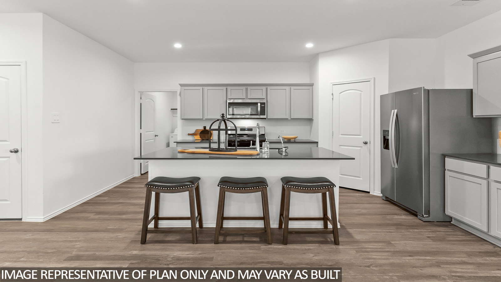 Open kitchen with an island, stainless steel appliances, light gray cabinets, white countertops, white walls, and vinyl wood flooring.
