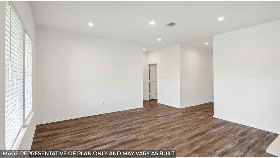 Large, open living room with white walls, windows, and vinyl wood flooring.