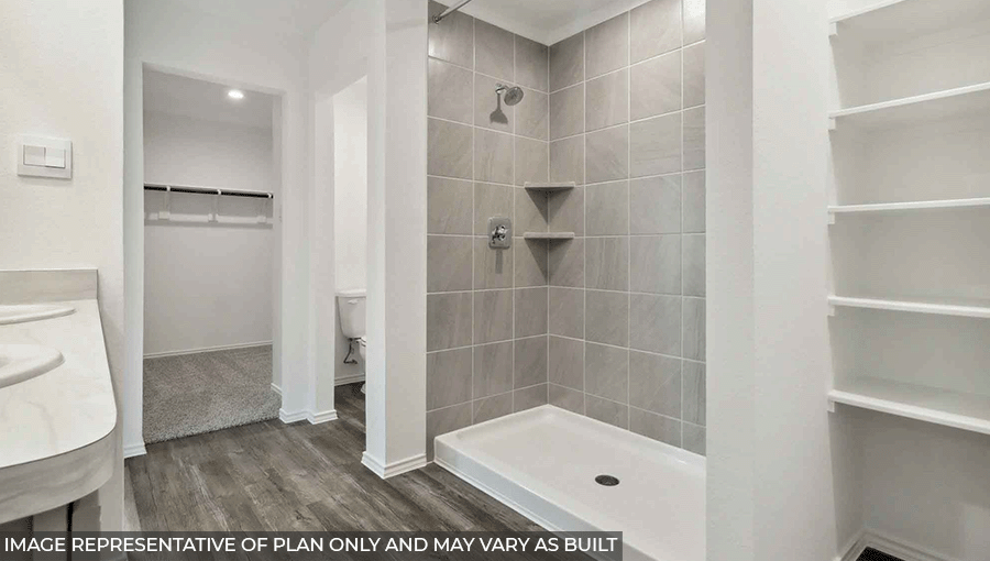 Primary bathroom with a walk-in shower, storage shelves, dual sinks, light gray cabinets, white walls, and vinyl wood flooring.