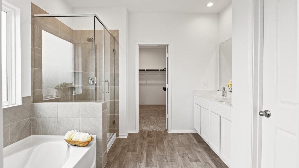 Primary bathroom with dual sinks, shower, tub, white walls, and vinyl wood flooring.