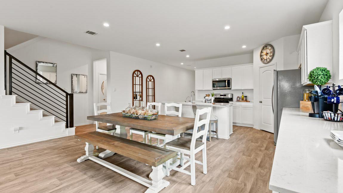 Staged dining area and kitchen with stainless-steel appliances, an island, and a tall pantry.