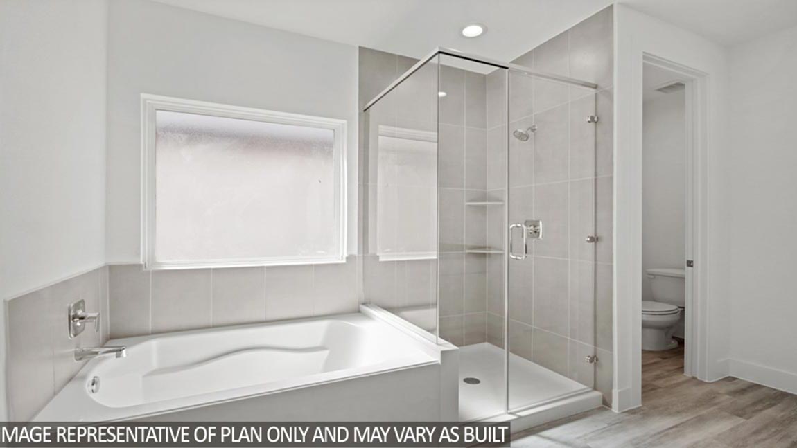 Primary bathroom with a tile tub, a standing shower with a glass door, and a frosted window.