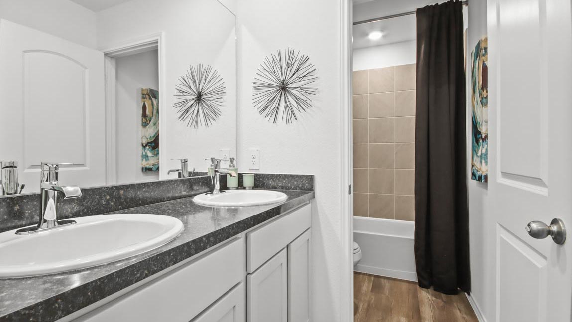 Secondary bathroom with a double sink and a separate room consisting of a tile tub/shower combo and a toilet.