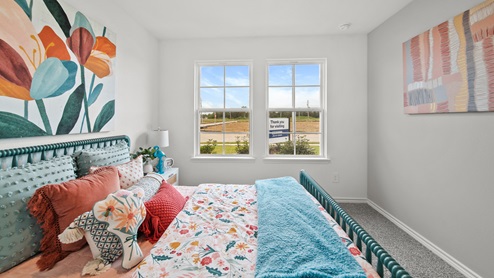 Reserve at Mallard Lakes model home secondary bedroom with colorful bedding accents and carpet flooring.