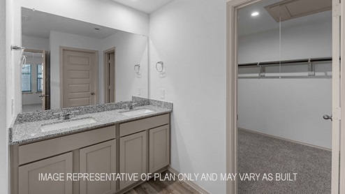 Cali primary bathroom with dual vanity sinks with granite countertops and walk-in closet.