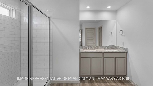 Cali primary bathroom with dual vanity sinks with granite countertops and walk-in shower.