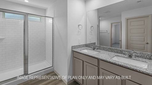 Cali primary bathroom with dual vanity sinks with granite countertops and walk-in shower.