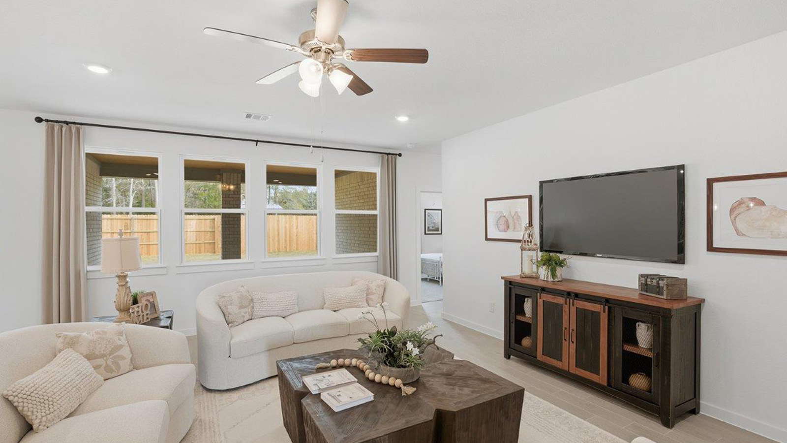 The woods model home living room with windows for natural lighting and view of secondary bedroom.