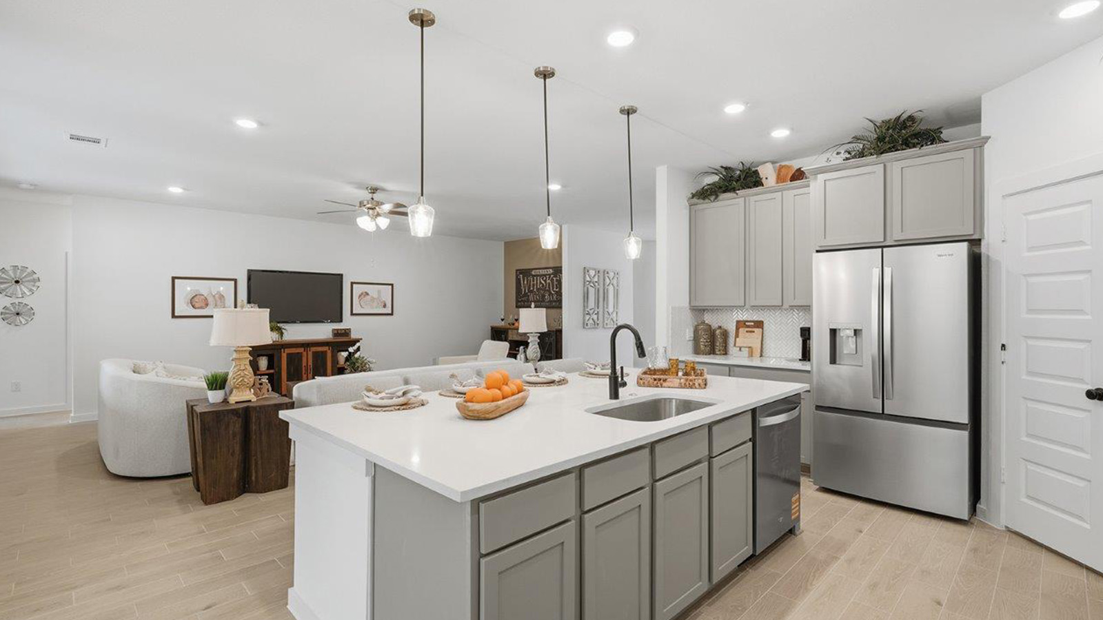 The woods model home kitchen with kitchen island and grey cabinets and view of open concept living room.