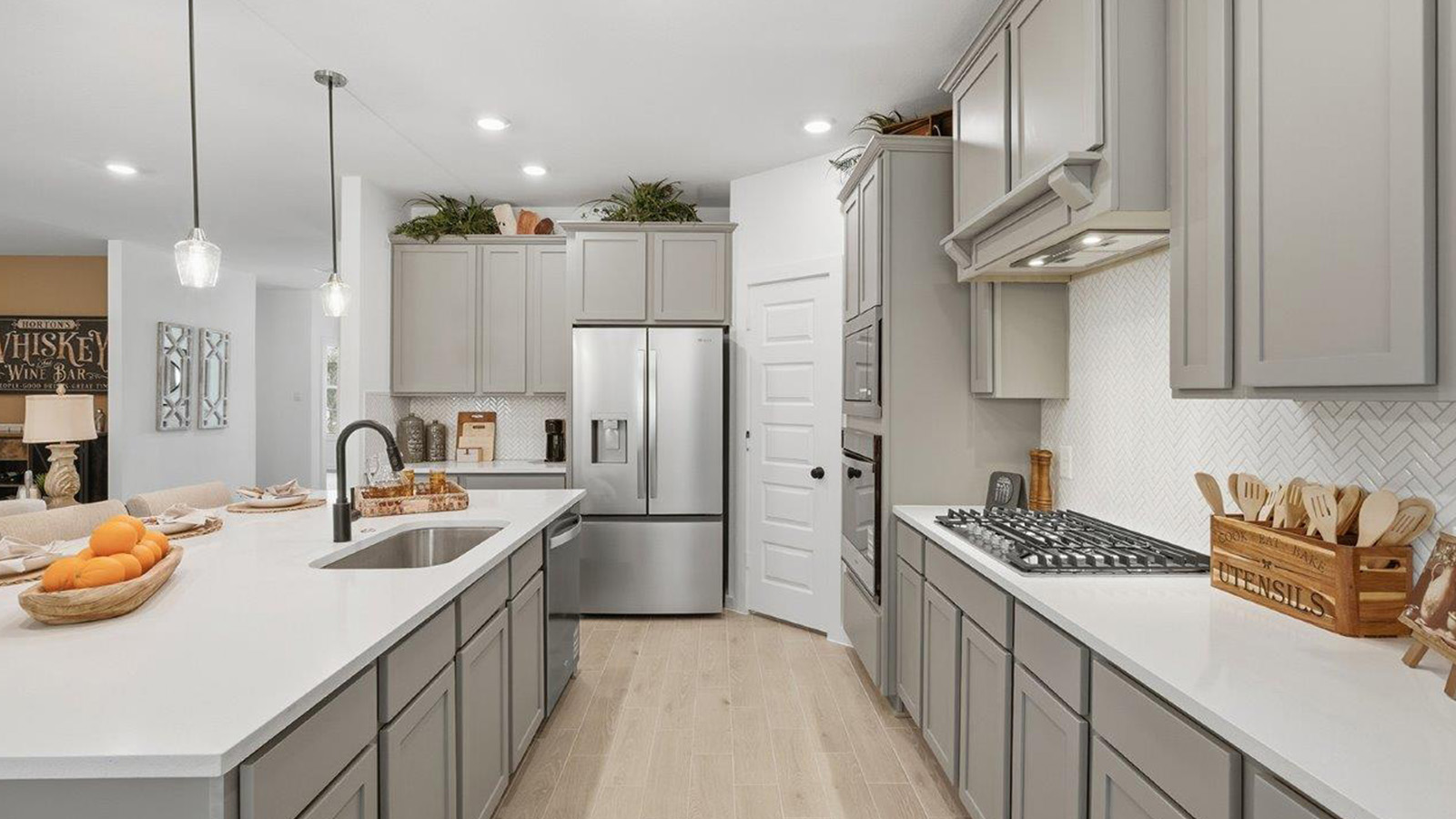 The woods model home kitchen with grey cabinets and light granite countertops.