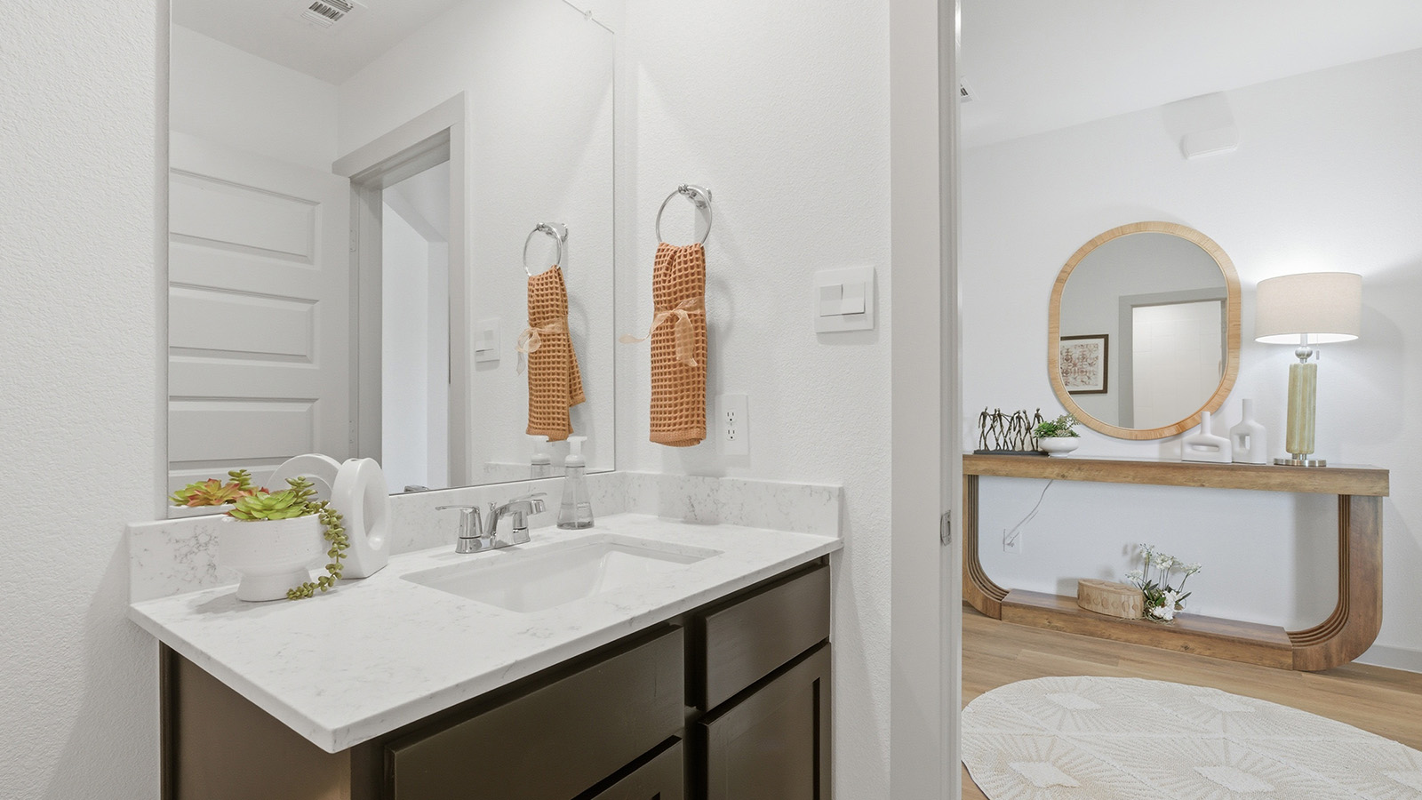Highland Village model home secondary bathroom with vanity sink and view of front entry hallway.