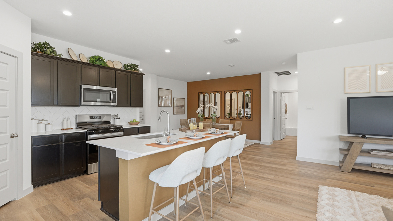 Highland Village model home kitchen with kitchen island and dark cabinets and light countertops with view of dining room.