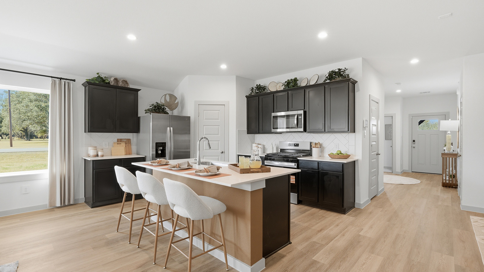 Highland Village model home kitchen with dark cabinets and light countertops with view of front entry way.