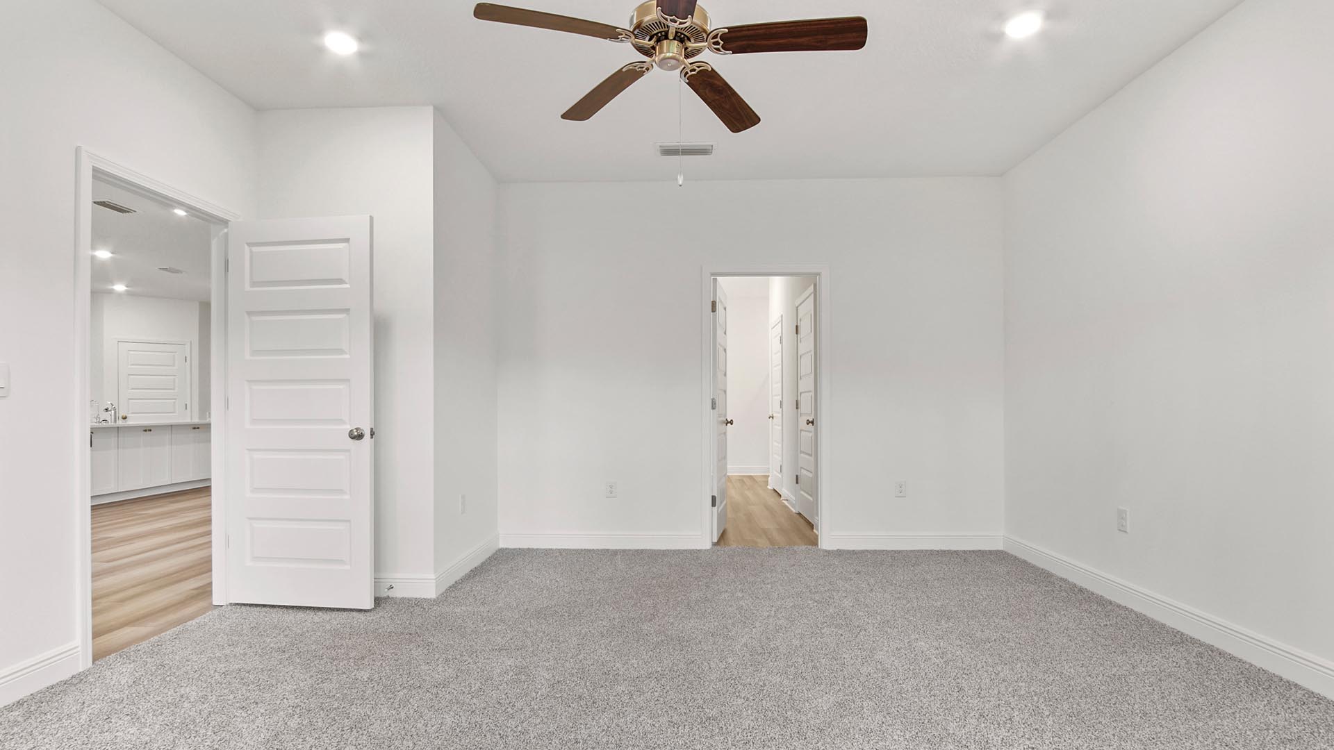 Primary bedroom with carpet flooring and ceiling fan and entrance to attached bathroom.