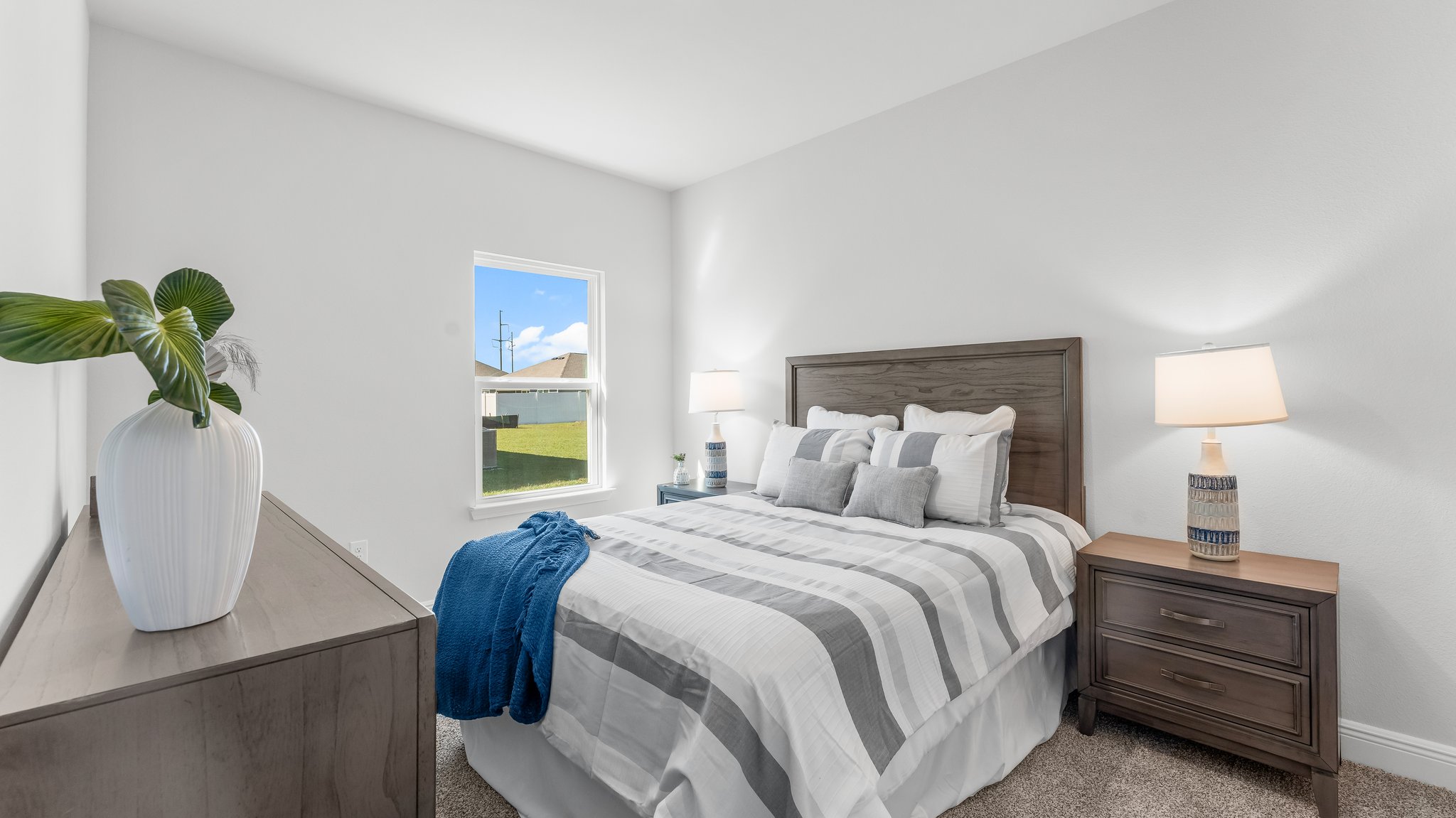 This image shows a staged guest bedroom with queen size bed a dresser and two night stands