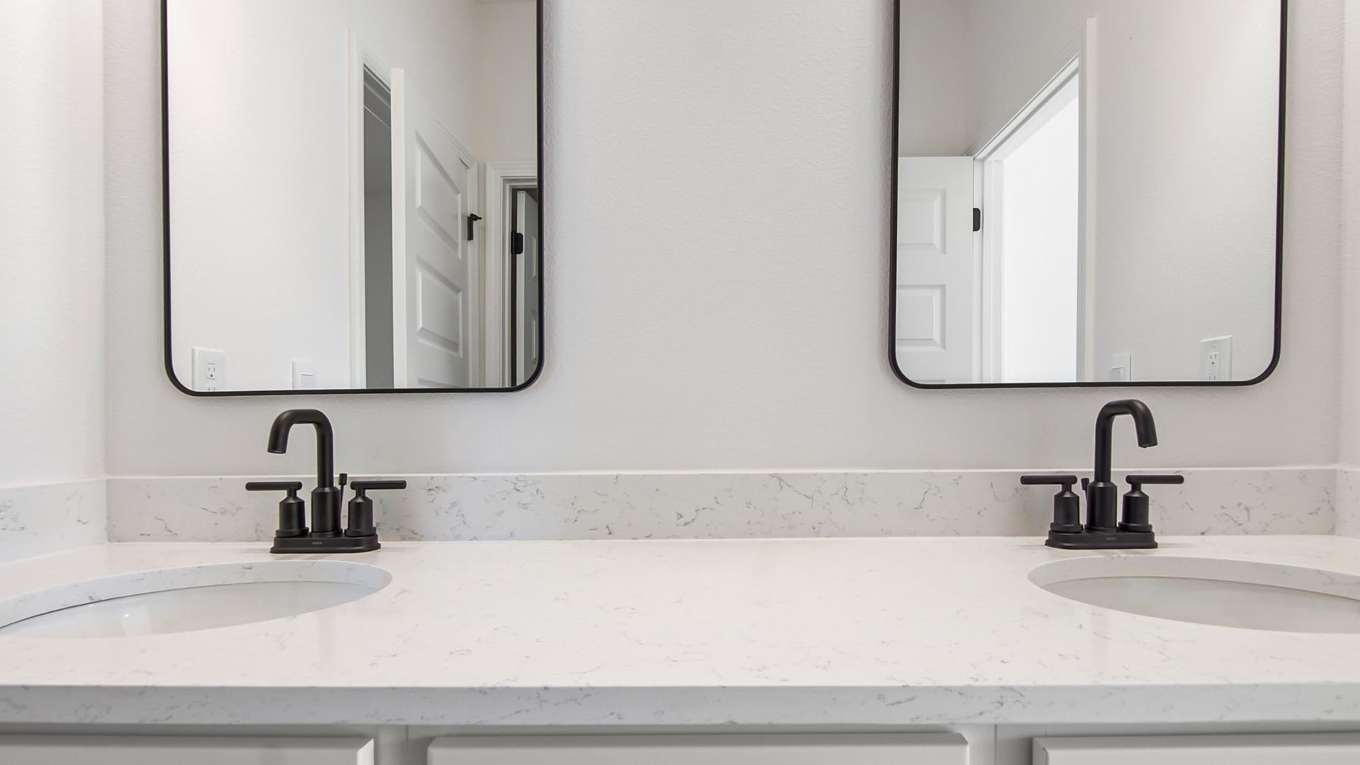 The dual sink vanity has separate mirrors over each sink and lower cabinetry for storage with matte black plumbing fixtures
