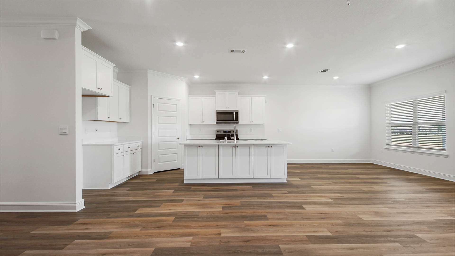 Open kitchen with island with white cabinets and quarts countertops and pantry and EVP flooring.