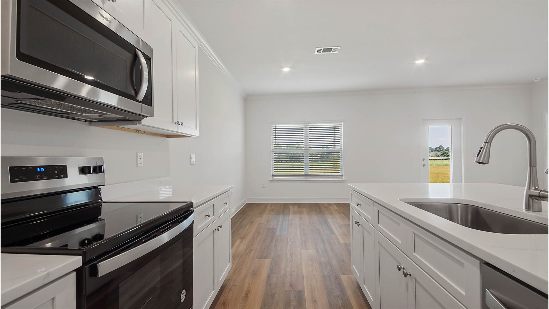 Open kitchen with EVP flooring and white cabinetry and stainless-steel appliances.