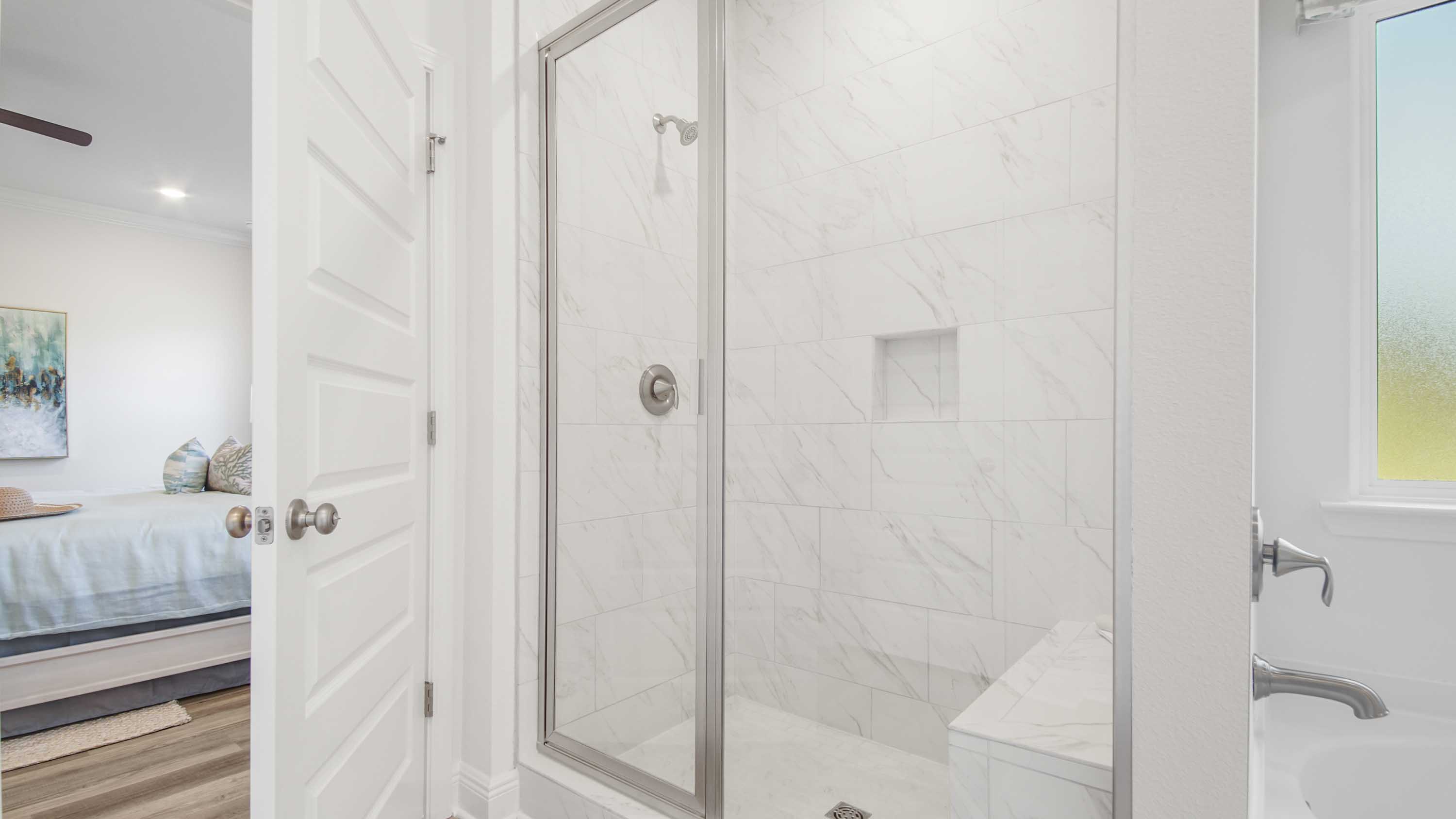 Primary bathroom soaking tub below frosted glass window and next to tile shower.