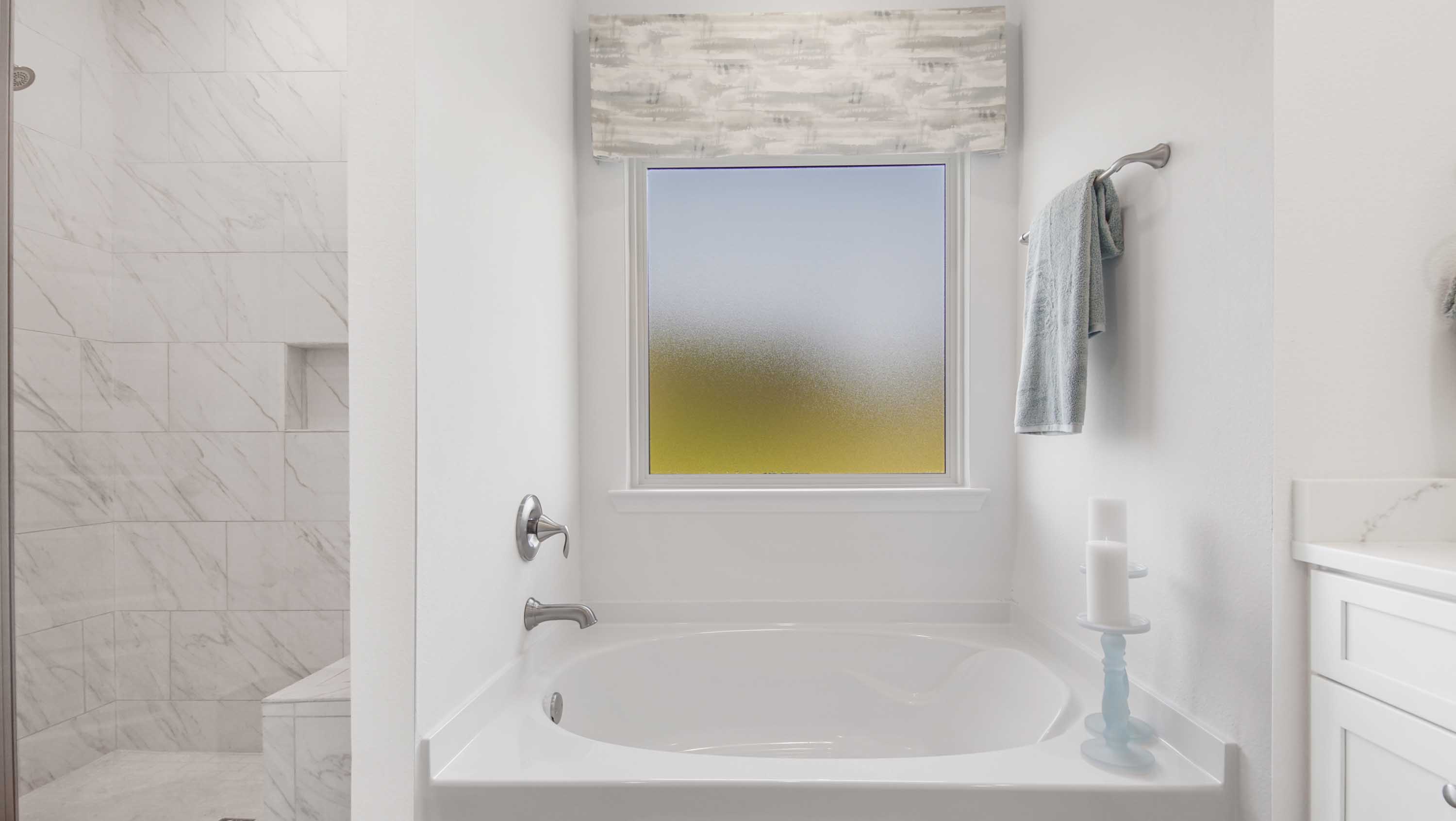 Primary bathroom soaking tub below frosted glass window and next to tile shower.