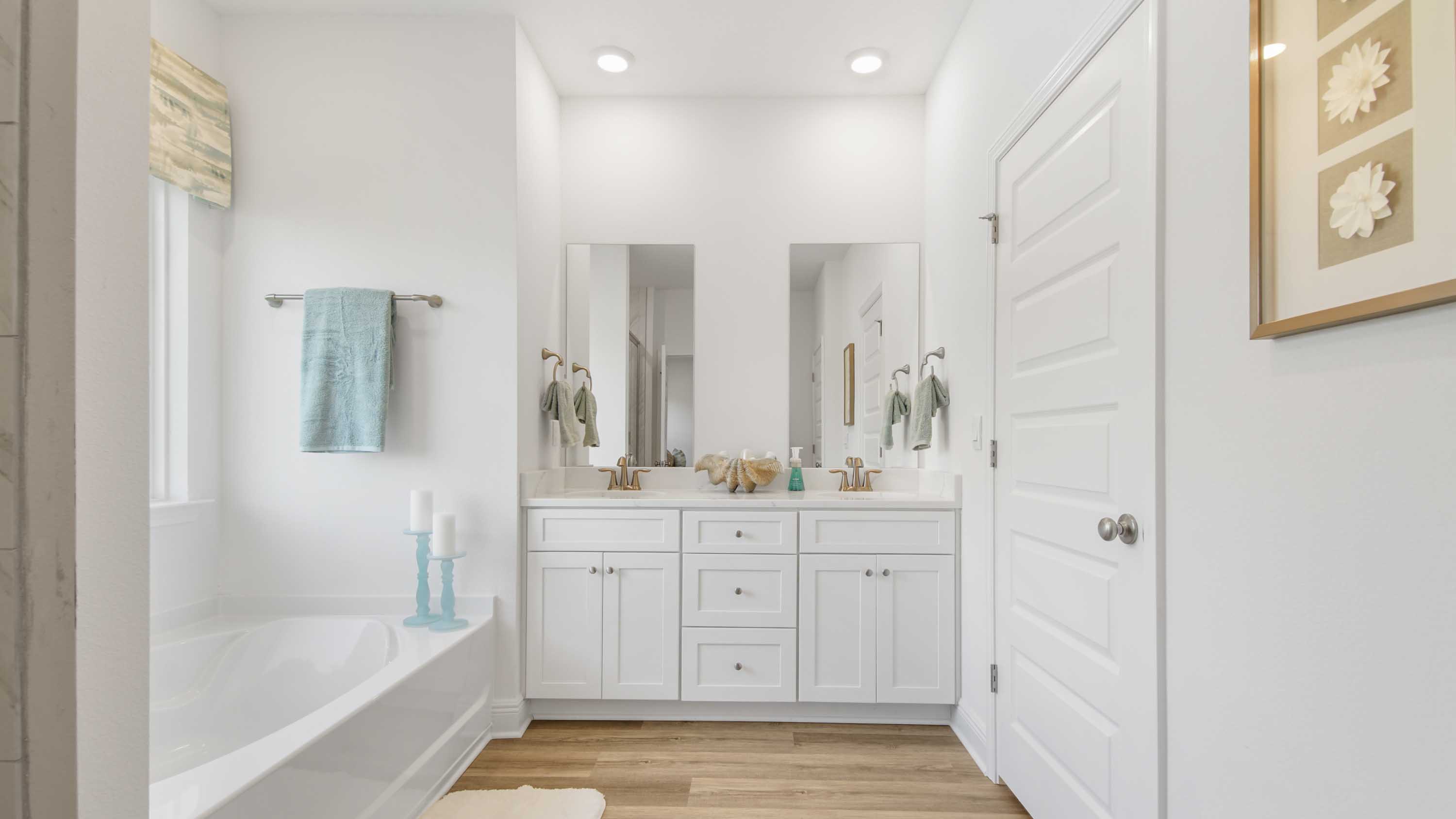 Primary bathroom with double sink vanity and quartz countertops and white cabinetry and two mirrors.