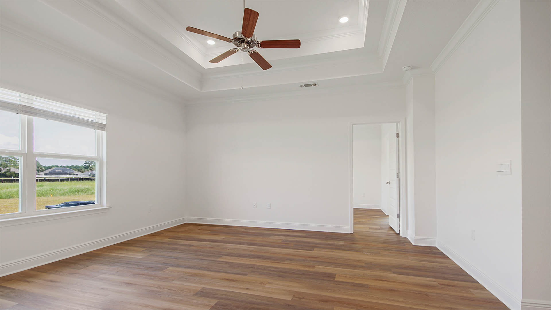 Living room with EVP flooring and large window and tray ceilings and ceiling fan.