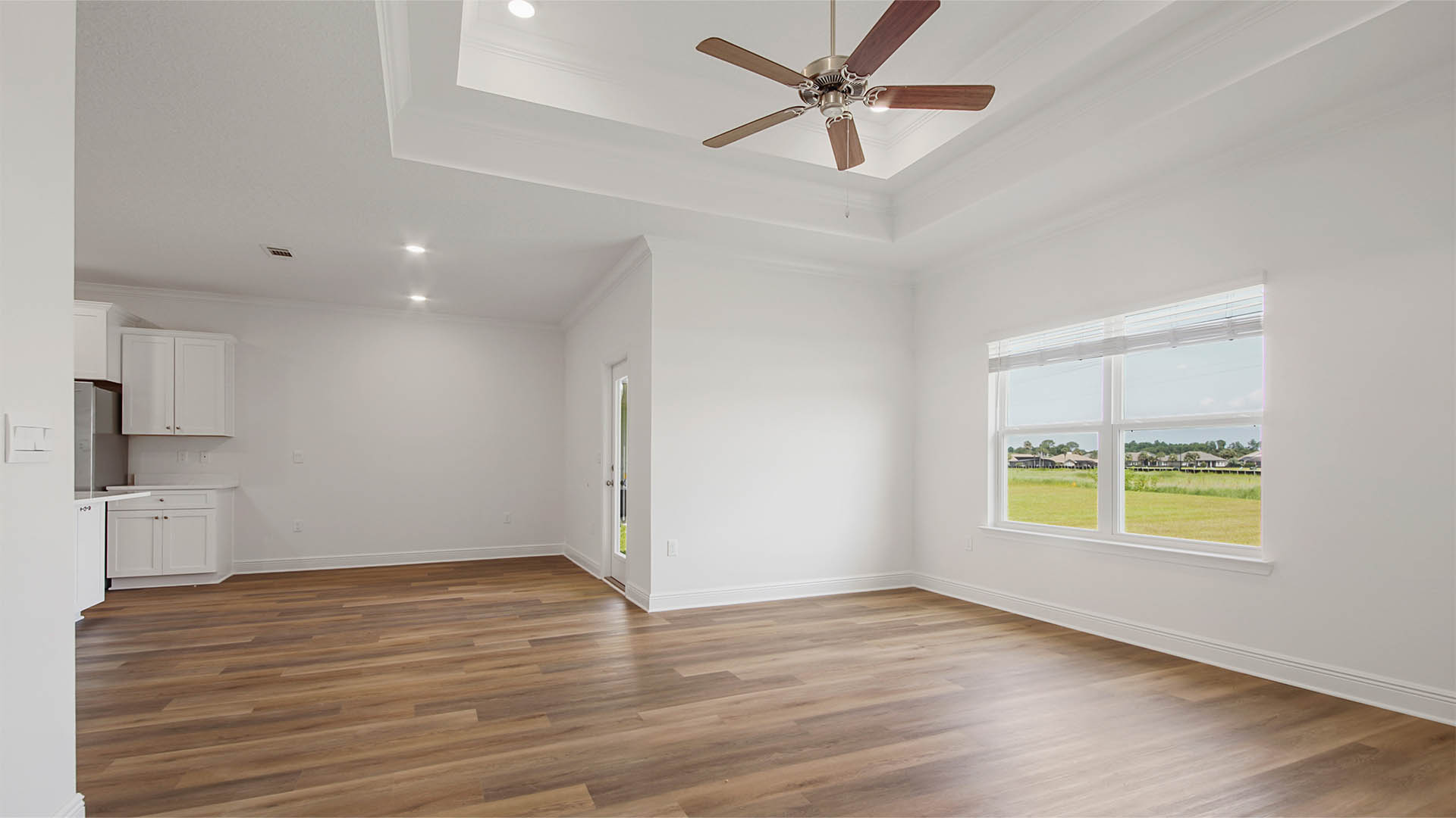 Living room with EVP flooring and large window and tray ceilings and ceiling fan.