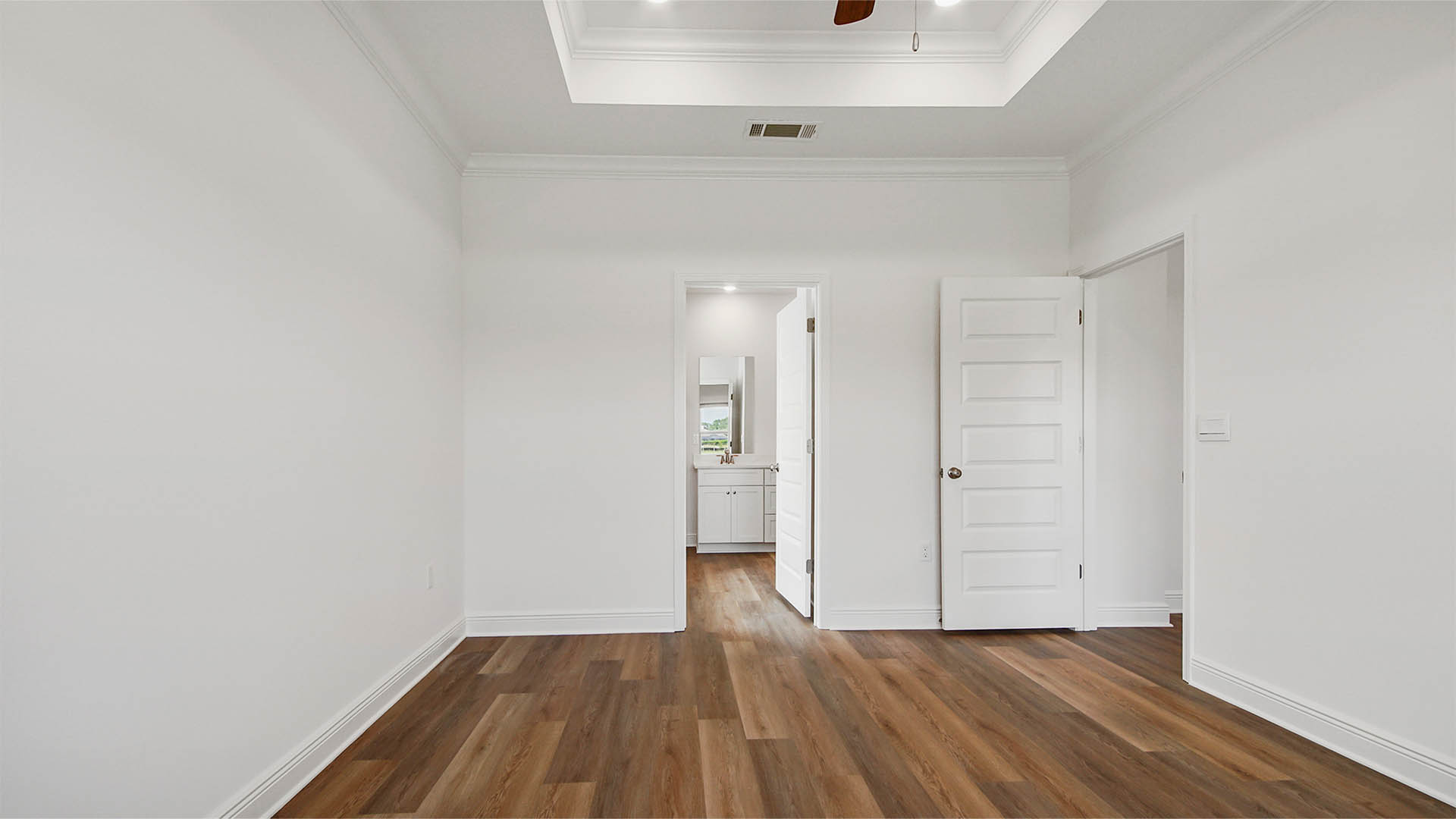Primary bedroom with EVP flooring and tray ceilings and bathroom entrance.