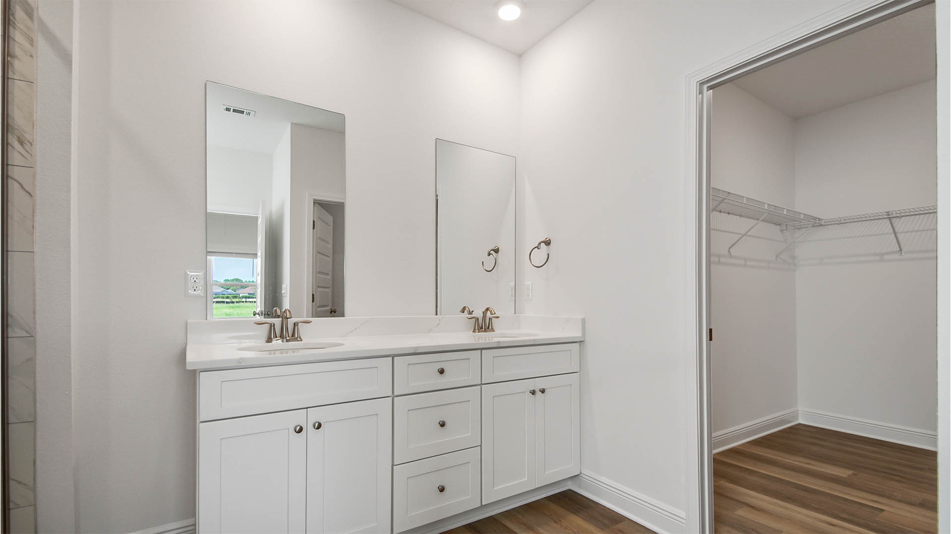 Primary bathroom with double vanity with white cabinetry and quartz countertops and large closet.